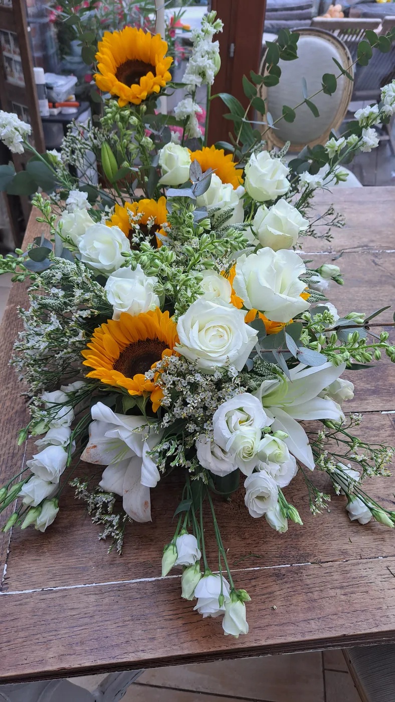Composition d’hommage allongée avec tournesols, roses blanches, lys et eucalyptus